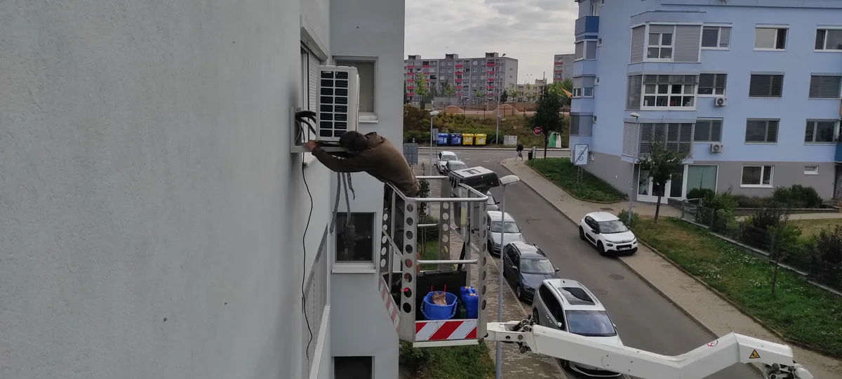 Technik instaluje venkovní klimatizační jednotku z montážní plošiny na panelový dům